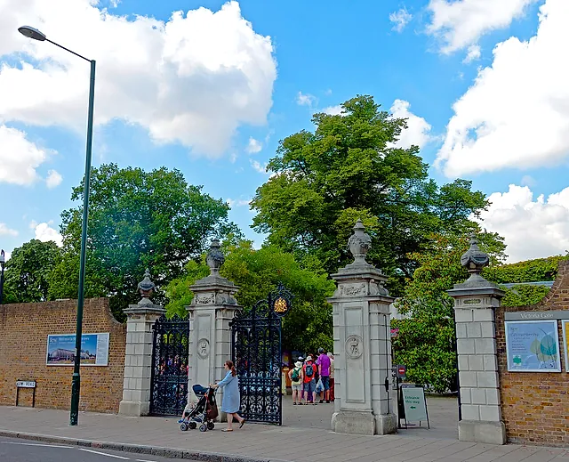 The stone gate piers and black wrought-iron gates of Victoria Gate, the main entrance, under a blue sky