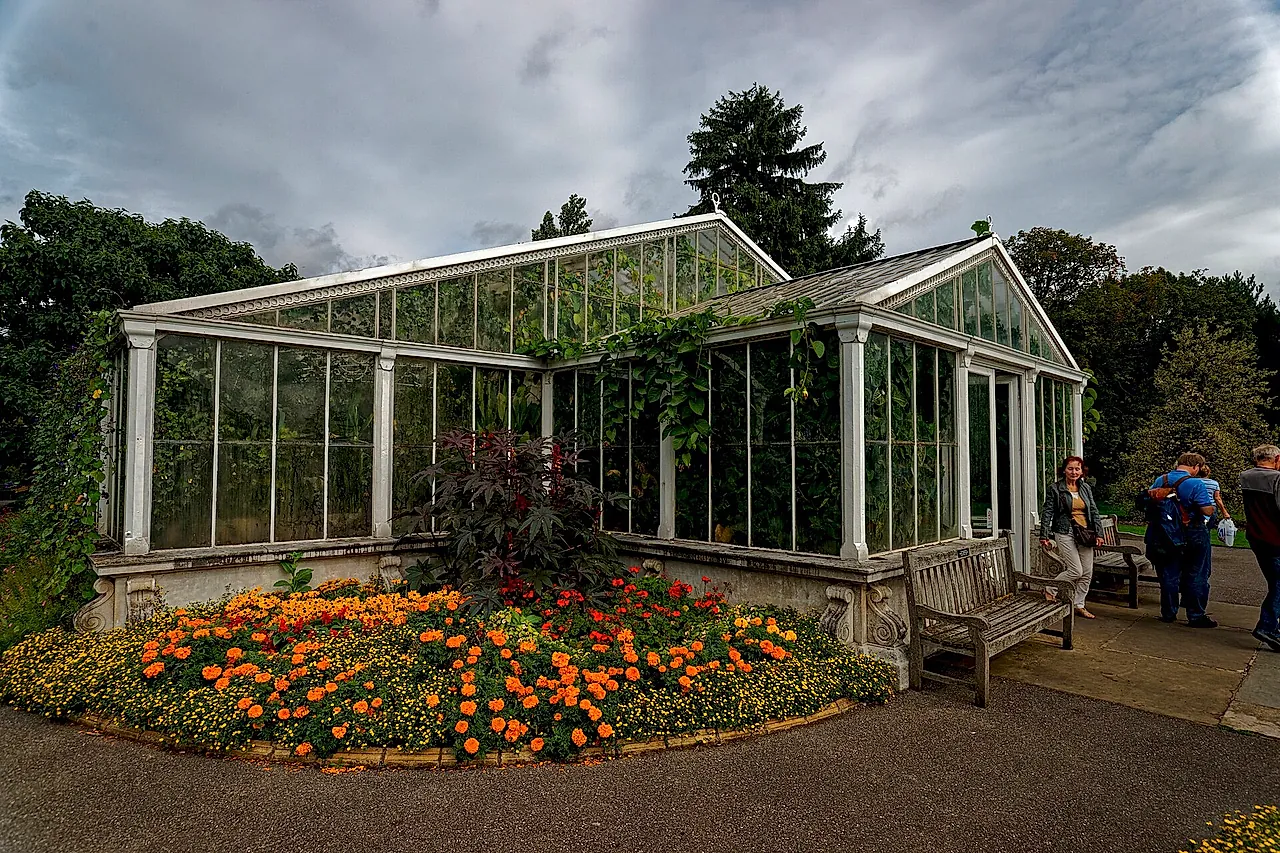 The glass Waterlily House with a bed of orange marigolds at its foot and a cloudy sky